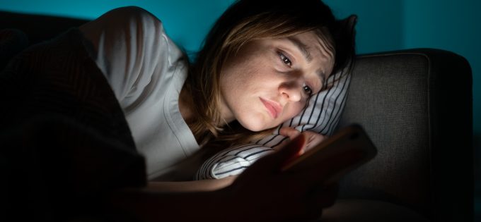 Woman using mobile phone while lying in bed at night, suffering from post breakup insomnia. Anxiety.